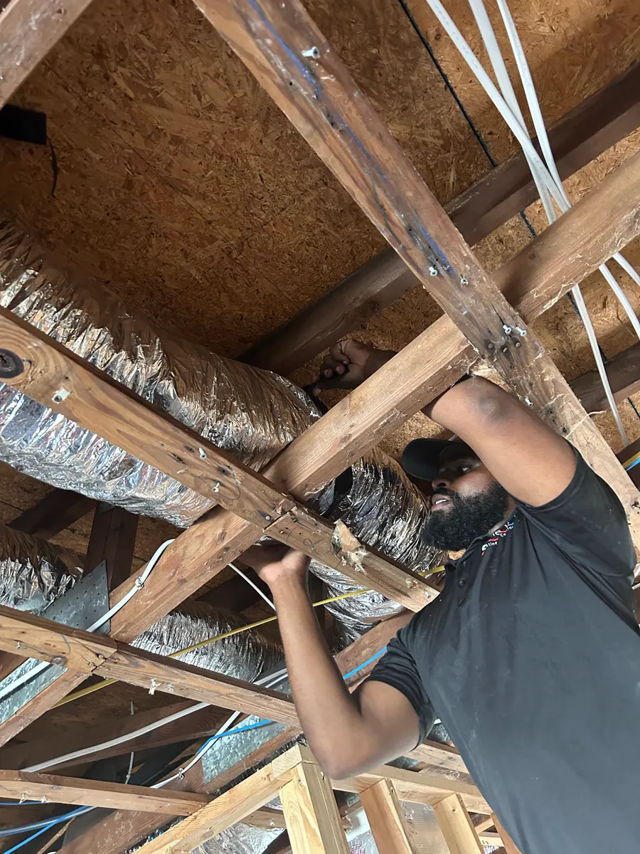 A technician running insulated ductwork in an attic